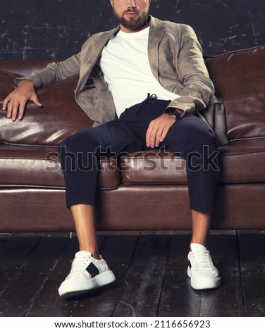 Man sitting on leather sofa wearing suit. Wearing snickers shoes