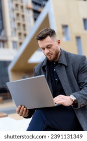 A man sitting on a ledge using a laptop computer. The Focused Man: Balancing Work and Serenity on a Ledge Overlooking the Cityscape
