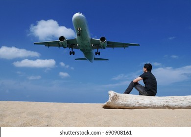 A man sitting on a log while air plane is landing on the beach at Mai Khao Beach, Phuket, Thailand