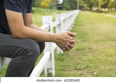 Man sitting on long white fence and crossed his fingers.