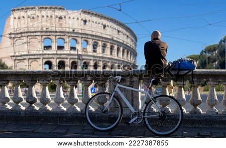 man sitting on low wall looks at the sea with bike in Rome with Colosseo