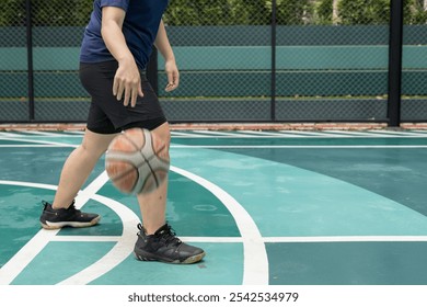 Man sitting on an outdoor basketball court, playfully tossing a basketball, enjoying a relaxed and casual moment. - Powered by Shutterstock