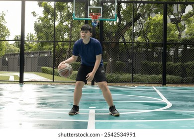 Man sitting on an outdoor basketball court, playfully tossing a basketball, enjoying a relaxed and casual moment. - Powered by Shutterstock