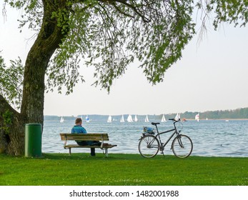 Man Sitting On Park Bench Watching Sailboats