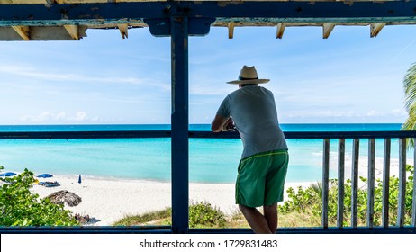 Man Sitting On The Patio Of An Old Decayed House On A Tropical Beach.
