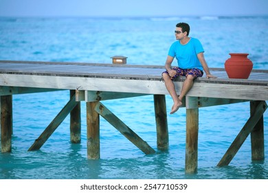 Man sitting on pier, Ocean view, Tropical vacation, Relaxing by the sea, Wooden dock, Summer holiday, Blue water, Beachside scene, Calm ocean,Outdoor leisure, Sunny day,Casual attire, Peaceful getaway - Powered by Shutterstock