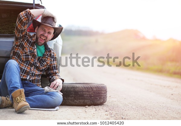 The\
man is sitting on the road by the car in the\
nature