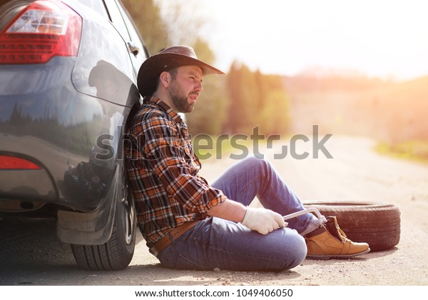 The\
man is sitting on the road by the car in the\
nature