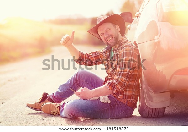 The
man is sitting on the road by the car in the
nature
