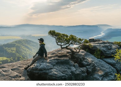 A man sitting on a rock, admiring the sunset in the mountains. Saxon Switzerland, Germany - Powered by Shutterstock