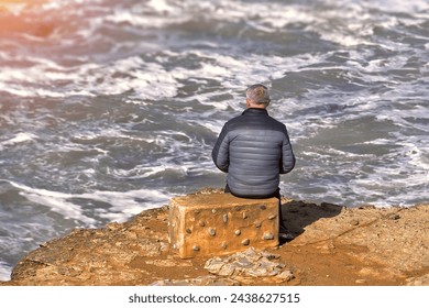 Man sitting on a rock by the sea and looking at the sea - Powered by Shutterstock