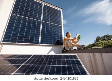 Man sitting on a rooftop and using digital tablet monitoring production from the solar power station installed on his property. Concept of modern technologies and sustainable lifestyle