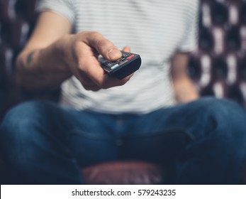 A Man Sitting On A Sofa Is Changing Channel With A Remote Control