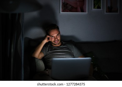 Man Sitting On The Sofa In The Dark In Pajamas With A Computer