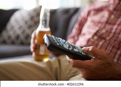 Man Sitting On Sofa Holding TV Remote And Bottle Of Beer