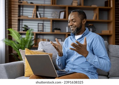 Man sitting on sofa at home, joyful african american man smiling using laptop for video call, talking with friends and colleagues remotely. - Powered by Shutterstock