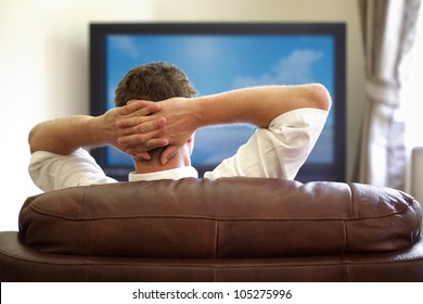 Man Sitting On A Sofa Watching Tv With Hands Folded Behind His Head