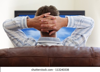 Man Sitting On A Sofa Watching Tv With Hands Folded Behind His Head