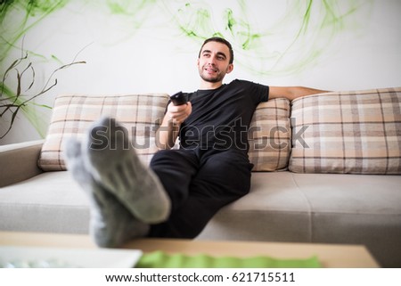 Man sitting on a sofa watching tv holding remote control