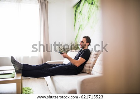 Man sitting on a sofa watching tv holding remote control