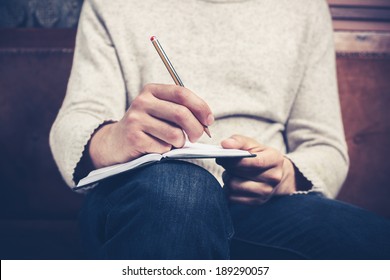 A Man Is Sitting On A Sofa And Writing Notes In A Notebook