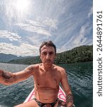 Man sitting on a stand up paddle board in the scenery of Lake Levico in Trentino in northern Italy. The man is forty years old and is a caucasian with light eyes and hair