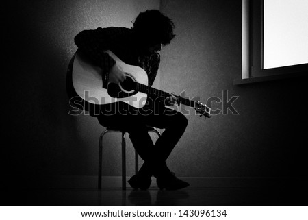 Man sitting on stool in dark room playing guitar