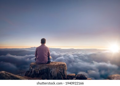 Man sitting on a summit above the clouds during sunrise