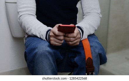 Man Sitting On The Toilet And Watching His Cell Phone