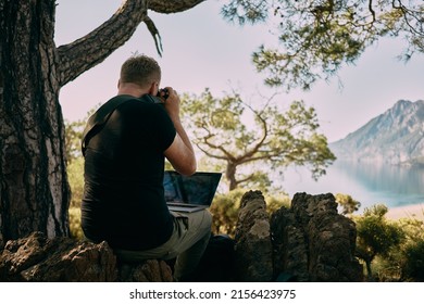 Man Sitting On The Top Of Mountain And Taking Photo Straight To Laptop. Remote Worker. High Quality Photo