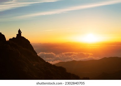 Man Sitting On Top Of Mountain Above Clouds Meditating After Hike Outdoors At Sunset. Back View Of Unrecognizable Tourist Guy On Cliff Contemplating Stunning View. Wanderlust Concept