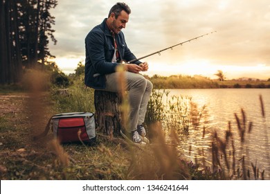 Man sitting on a tree trunk beside a lake with his fishing rod. Man enjoying his leisure time fishing in a lake. - Powered by Shutterstock