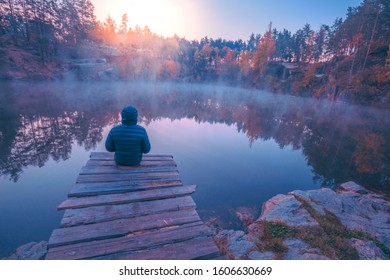 Man sitting on wooden deck and looking at lake with granite shore. Sunrise over the lake