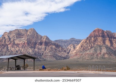 A man is sitting and reading in front of amazing view of red stone mountains near the Red Rock Canyon with ancient rock formations can be seen from far away. Surrounding area is a vast meadow - Powered by Shutterstock