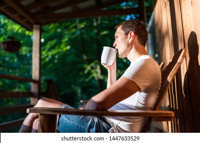 Man sitting relaxing on rocking chair on porch of house in morning wooden cabin cottage drinking coffee from cup - Powered by Shutterstock