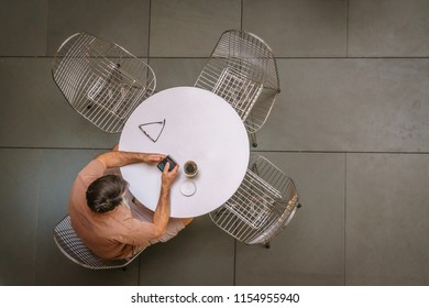 Man Sitting At Round White Table On Smart Phone With Coffee Seen From Above