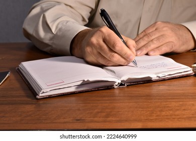 A man sitting at a table with a fountain pen writes something on the sheets of a notebook.
