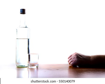 A man is sitting at a table, in front of him is a bottle of alcohol and an empty glass