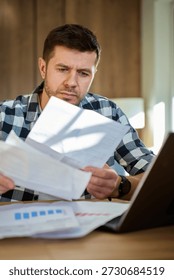 Man sitting at table at home checking bills and financial documents. Concept of household expenses, budgeting, payments and personal finance management
