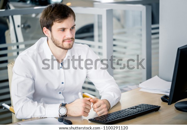 Man sitting at the table in the office.\
Monitor, car key and keyboard the\
desk.