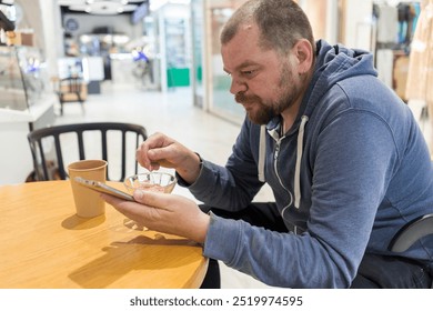 A man is sitting at a table with a tablet in front of him. He is eating a bowl of food and looking at his tablet
