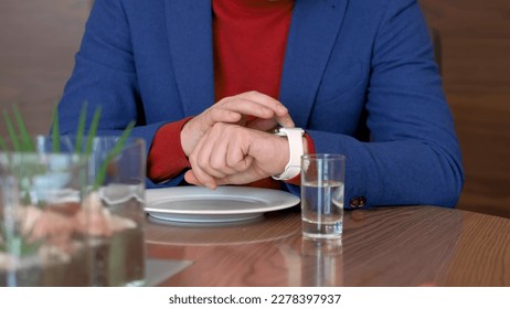 Man sitting at table and using mobile app in smart watch on hand while waiting food in cafe. Man setting smart clock on table in restaurant