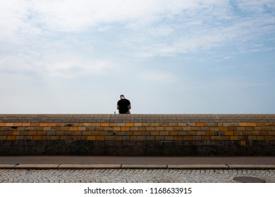 Man sitting at  a wall with his back to the camera and the sky above