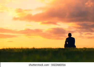 Man sitting watching sunset. Enjoying a peaceful moment, thinking, getting away from it all concept.  - Shutterstock ID 1022460316