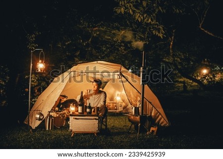 A man sitting in white camping tent in the forest at night with lantern lights and wood stove, it's night in the forest vibes