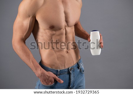 Man with six pack abs torso cropped view hold bottle of sport body wash grey background, bodywash.