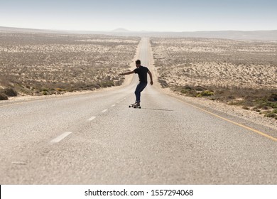 Man skateboarding downhill on a straight road in the dry Namibian Landscape - Shutterstock ID 1557294068