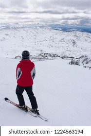 A Man Skier In A Red Jacket Standing On Top Of The Ski Slope And Looking Towards The Snow Covered Hills In Perisher Ski Resort, New South Wales, Australia