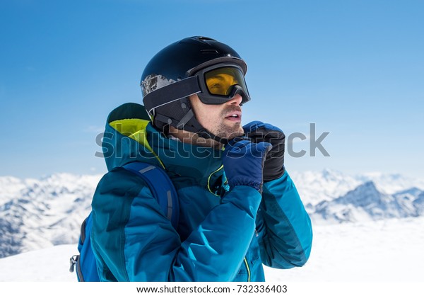 Man skier wearing helmet and ski mask on\
snowy mountain. Man getting ready for a ski trip in winter. Young\
skier looking at mountain covered by\
snow.