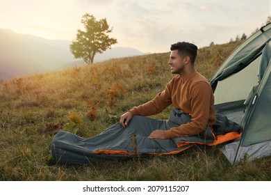 Man in sleeping bag near camping tent on hill - Powered by Shutterstock